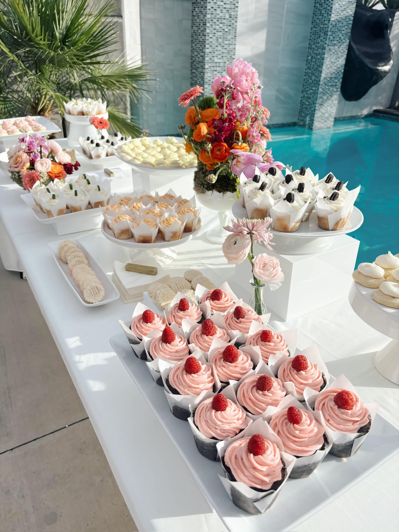 Poolside dessert table with colorful cupcakes and fresh flowers